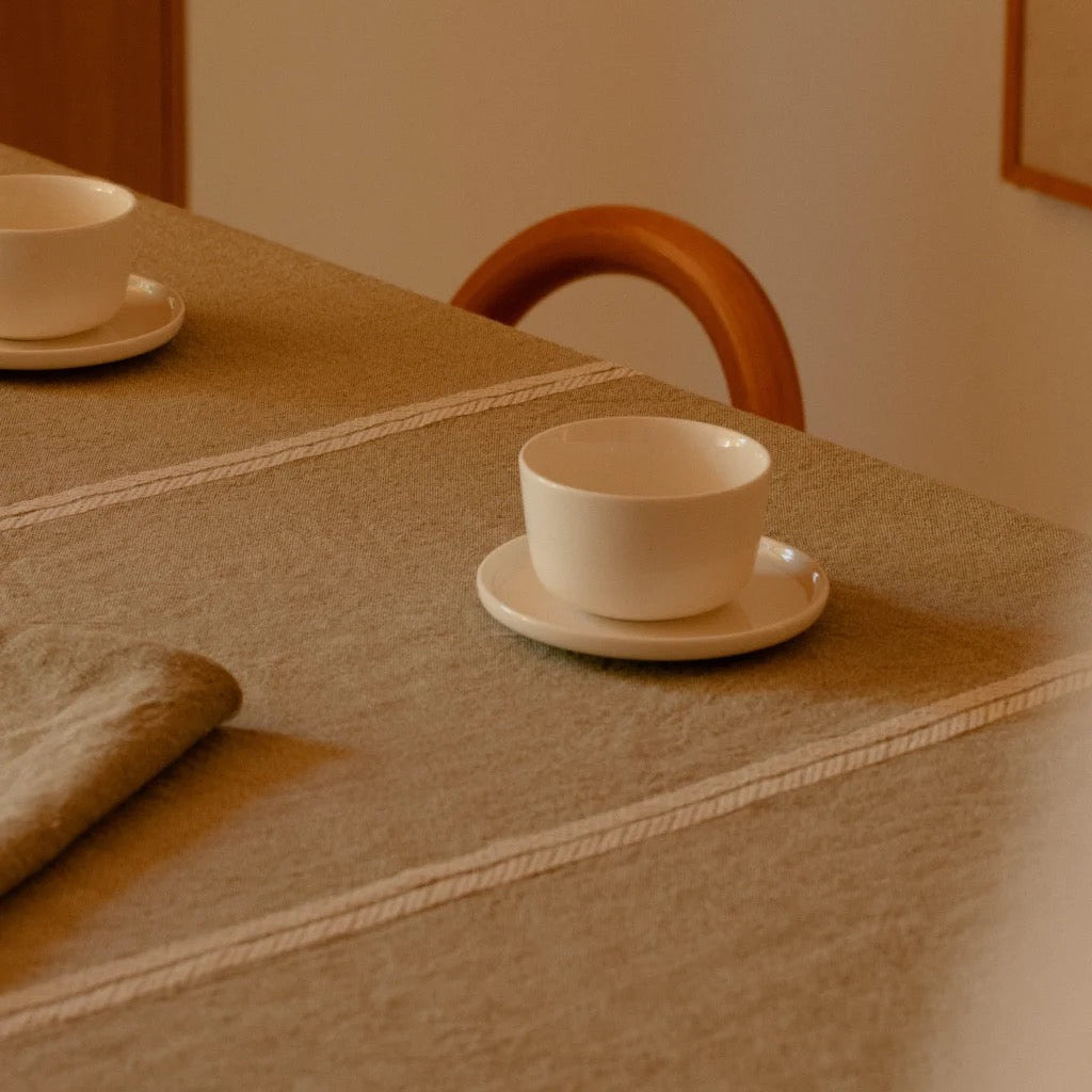 White teacup and saucer on a textured table with a wooden chair in the background.