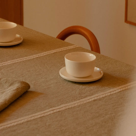 White teacup and saucer on a textured table with a wooden chair in the background.